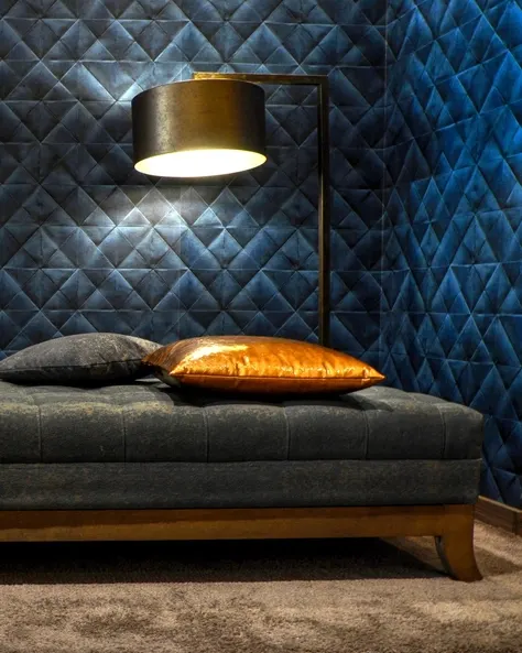 A floor lamp lit above a low sofa against a dark blue quilted wall