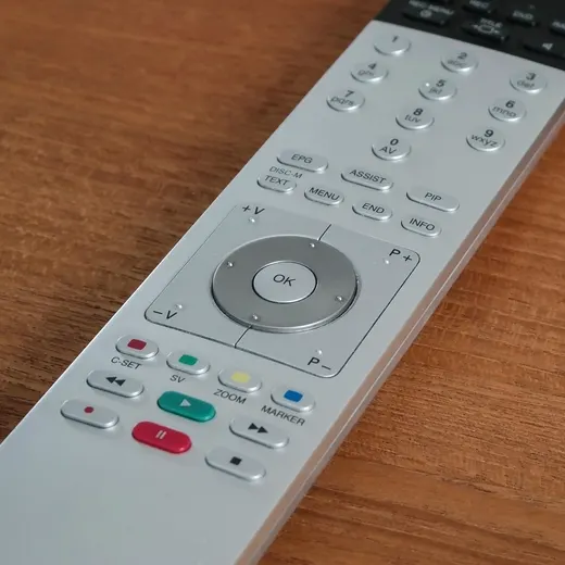 The round direction pad of a TV remote control, on a wooden table